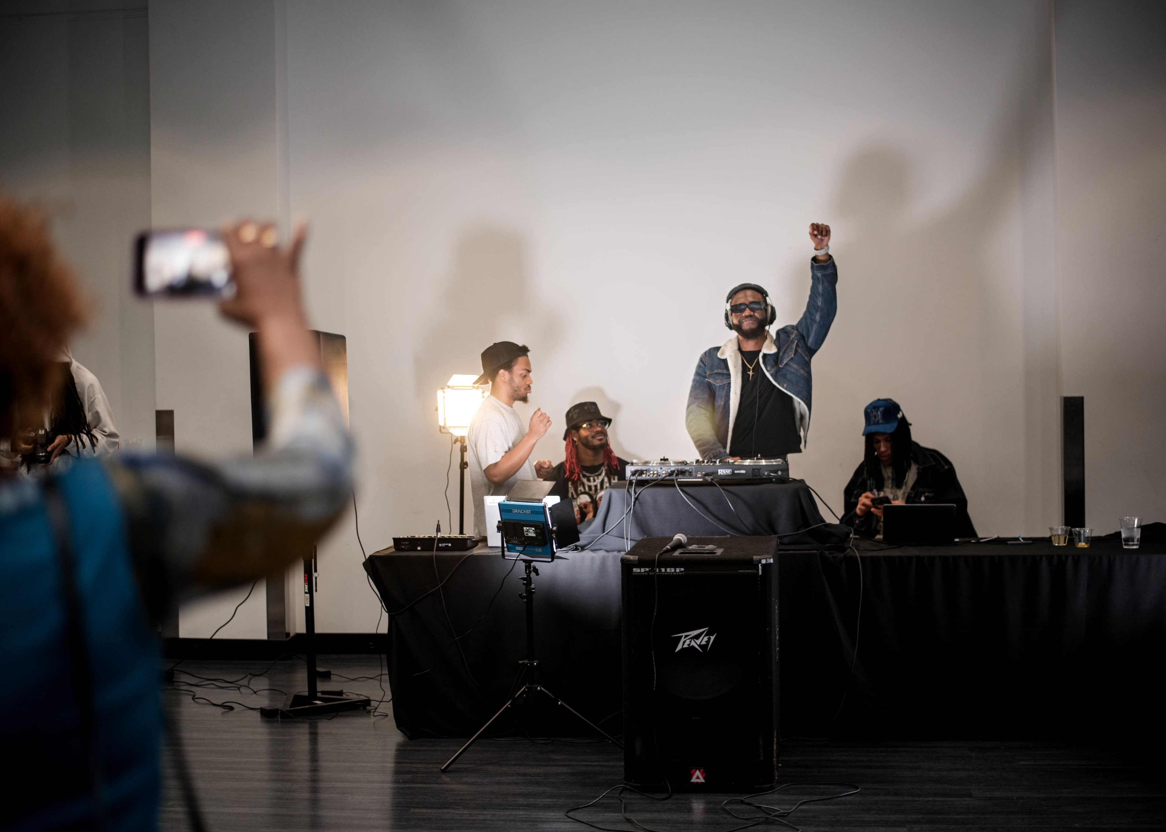 DJ raising a fist in the air during a live event, with other participants around, conveying energy and audience engagement.