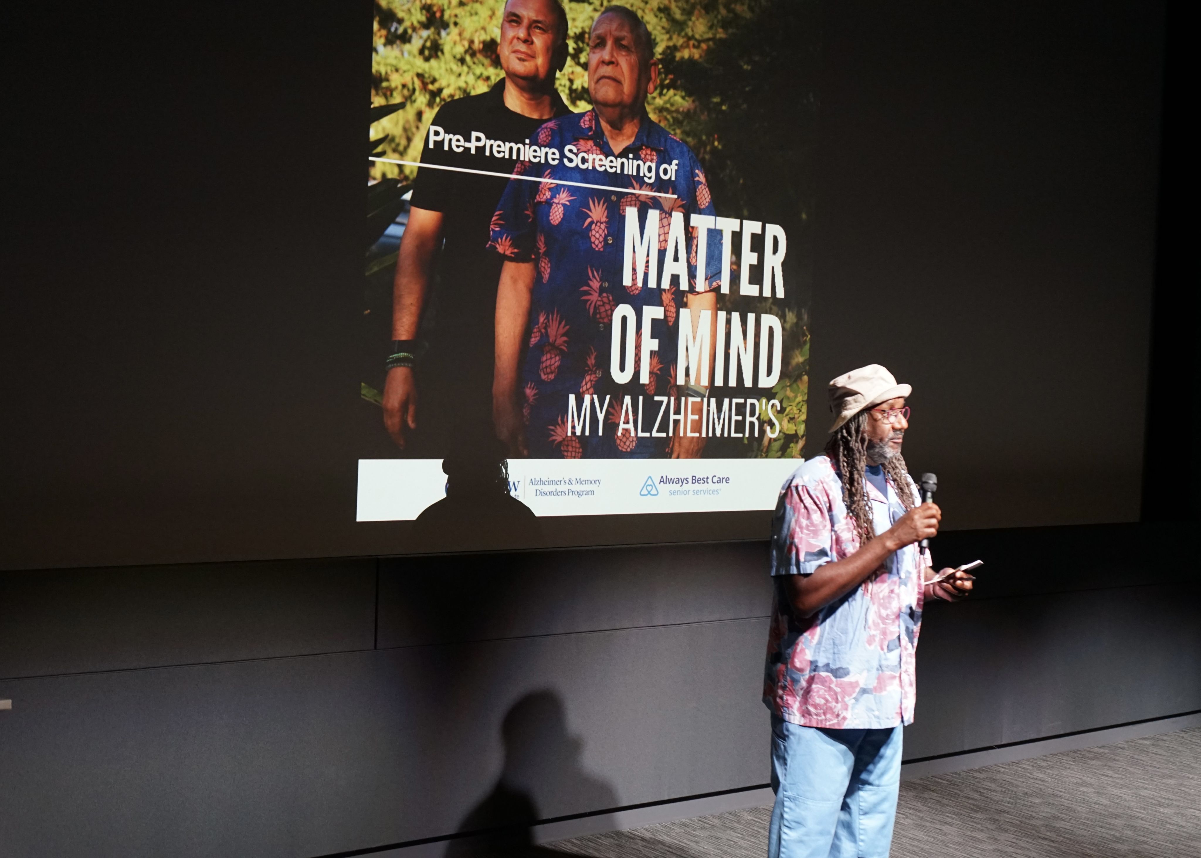 Image of a man speaking in front of a film poster.